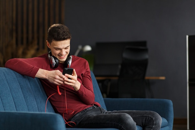 Enjoy listening to music.Young man in headphones listening music on smart phone using music app. Portrait of guy in earphones and mobile phone at home. Relaxation, leisure and stress management.