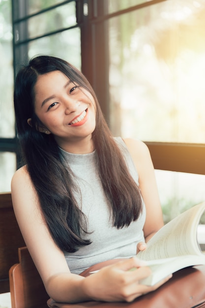 Goditi i momenti di relax con il libro di lettura, le donne asiatiche tailandesi sorridono con un libro nella caffetteria colorazione vintage