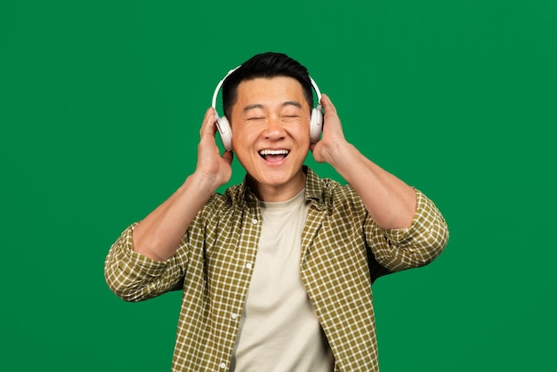 Enjoy the sound happy asian mature man wearing and touching wireless headset enjoying song with