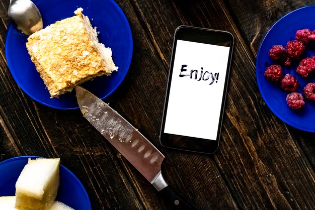 Enjoy text on a smartphone with sweet food on wooden table flat
lay concept f