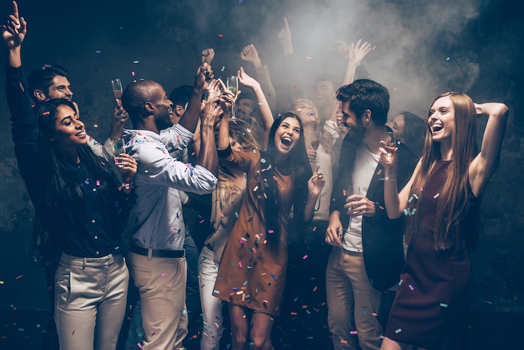Photo enjoying carefree time together. group of beautiful young people throwing colorful confetti and looking happy