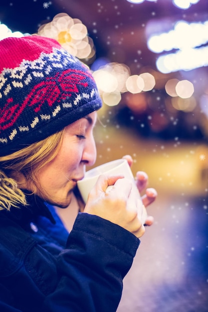 クリスマス マーケットでクリスマスの時間を楽しんでいる 若い女の子がグリュー ワインを飲んでいます。