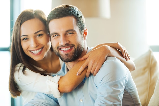 Foto godendo ogni minuto insieme. bella giovane coppia di innamorati seduti insieme sul divano mentre la donna abbraccia il suo ragazzo e sorride