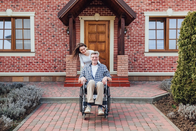 Enjoying in family time elderly man in wheelchair and smiling daughter in the garden