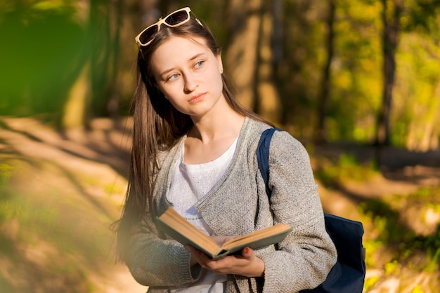 Наслаждаясь свободным временем Счастливая девушка читает интересную книгу в лесопарке