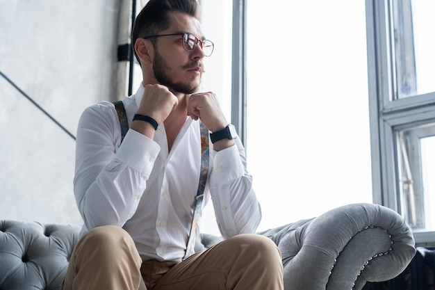 enjoying free time. thoughtful young man in full suit looking away while sitting on the sofa at home.