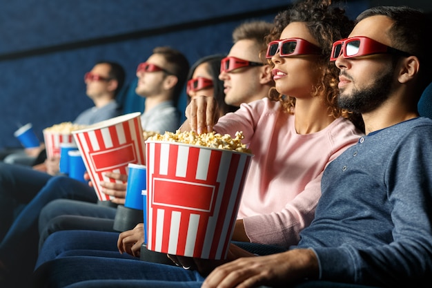 Enjoying a great movie. Shot of a group of friends watching a movie eating popcorn drinking beverages