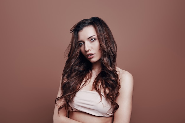 Enjoying her beauty. Attractive young woman looking at camera while standing against grey background