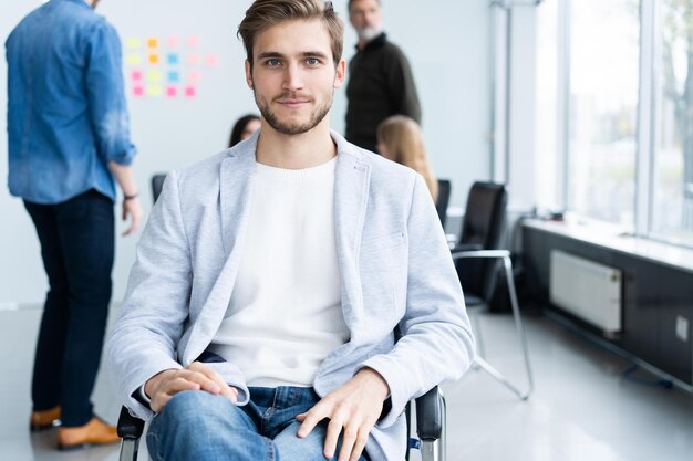 enjoying his work handsome young man looking at camera and smiling while his colleagues working in the background