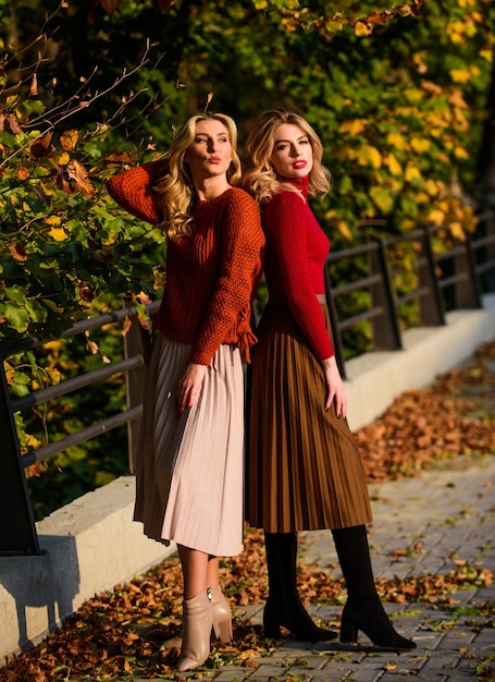 Enjoying life. autumn women outdoor. girl friends walk in park. sunny day with fallen leaves. fall fashion season. Pleated trend. girls in corrugated skirt and sweater. female beauty. real femininity.