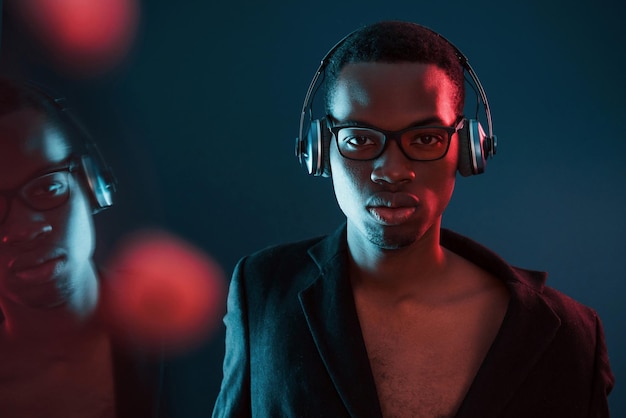 Photo enjoying listening music in headphones in glasses futuristic neon lighting young african american man in the studio