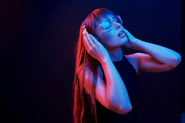 Enjoying the music. Studio shot in dark studio with neon light. Portrait of young girl