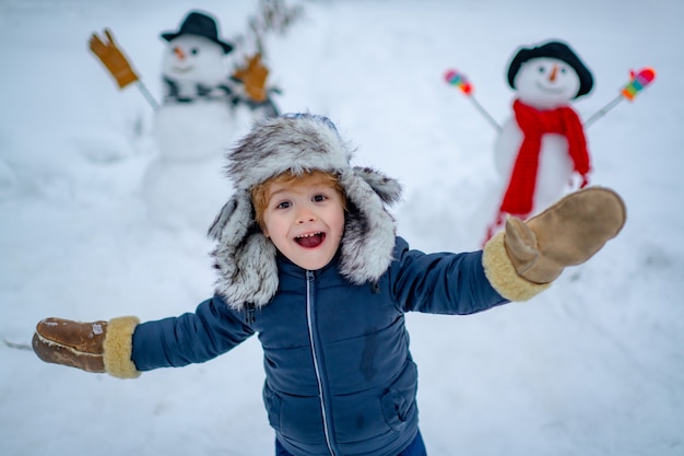 Enjoying nature wintertime winter kid funny boy posing on winter weather snowman and funny little bo...