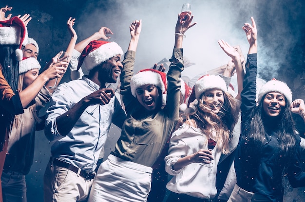 Enjoying New Year party. Group of beautiful young people in Santa hats dancing and looking happy