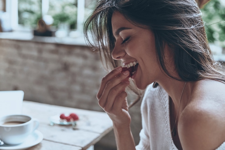Photo enjoying nice breakfast. attractive young woman keeping eyes closed and eating raspberries 