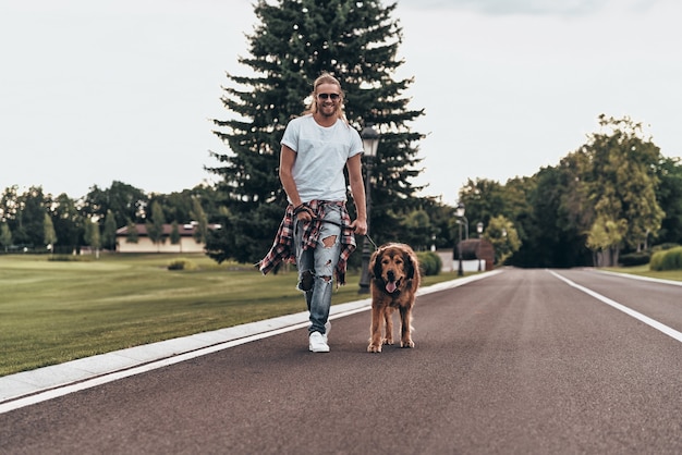 Enjoying nice day. Full length of handsome young man walking with his dog while spending time outdoors