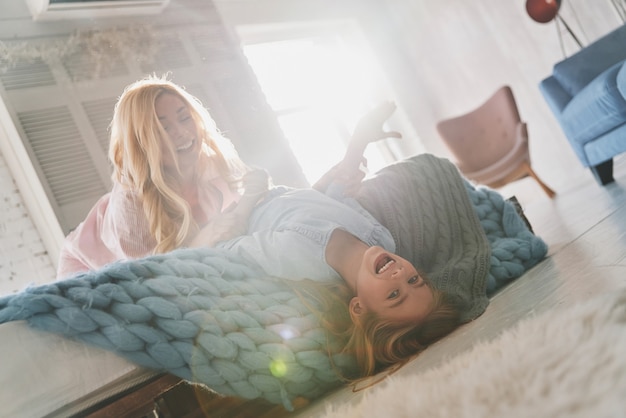 Enjoying playtime! Beautiful young mother going crazy with her cute daughter and smiling while sitting on the bed at home