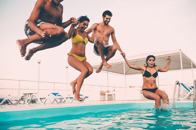 Godendo insieme festa in piscina. gruppo di bei giovani che sembrano felici mentre saltano insieme in piscina