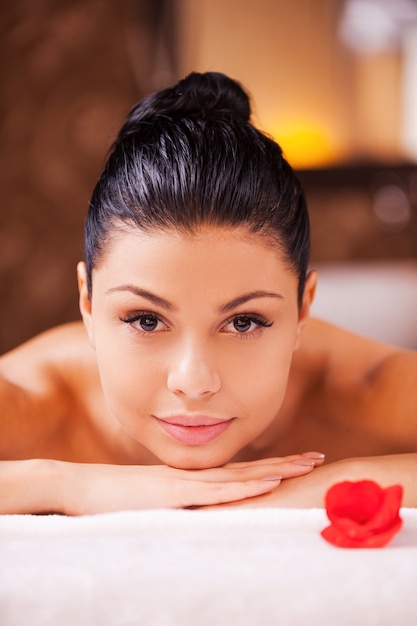 Enjoying relaxation. Front view of beautiful young shirtless woman lying on massage table and looking at camera