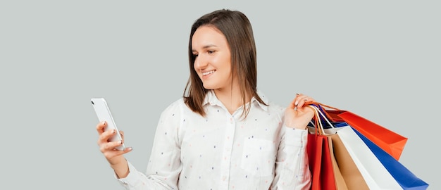 Enjoying shopping online with smartphone Young woman using phone and holding paper shopping bags