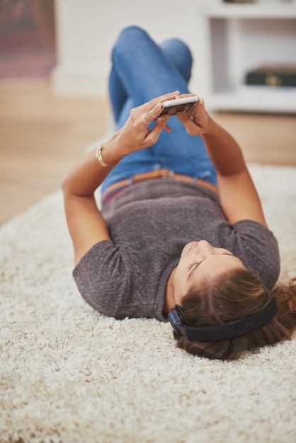 Enjoying some soft soothing music Shot of a young woman relaxing at home and listening to music on her phone