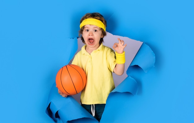 Фото Наслаждаясь спортивной игрой маленький баскетболист с баскетбольным мячом показывает знак ok мальчик в спортивной одежде