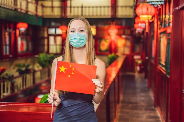 Enjoying vacation in china young woman in medical mask with a chinese flag on a chinese background