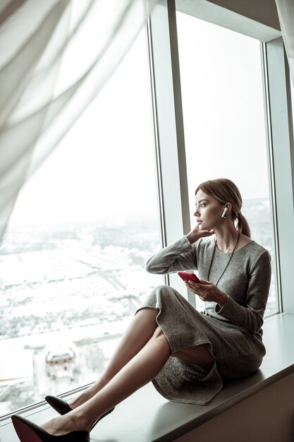 Enjoying the view. Slim stylish woman sitting near window and enjoying the view from her apartment