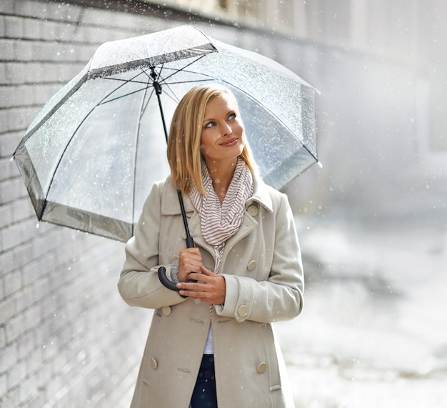 雨の中散歩を楽しむ雨の日に傘をさして通りを歩いている若い女性のショット