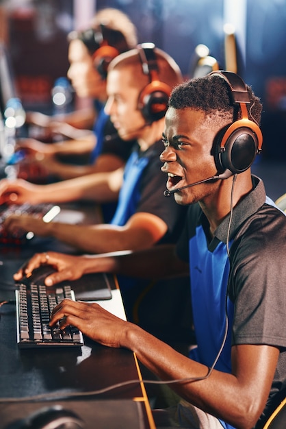 Enjoyment side view of a young excited african guy male cybersport gamer wearing headphones playing