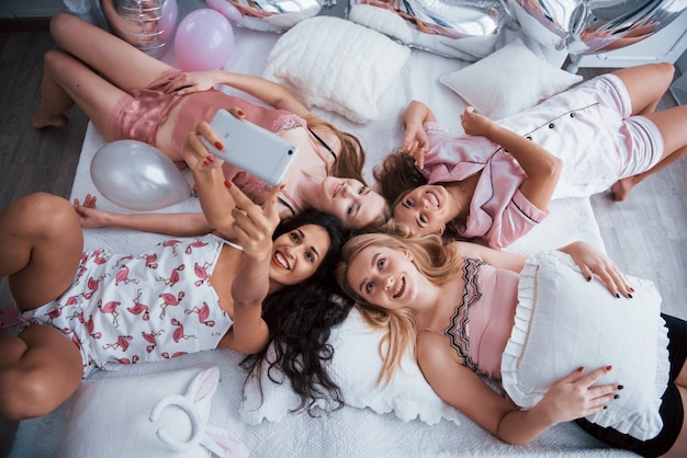 Enjoys meeting. Taking selfie with friends while lying on the bed at bachelorette party