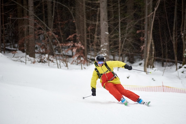 Enkele afdaling van jonge mannelijke skiër alpineskiën en carve beurt op hoge beboste helling. Skiën tijdens sneeuwval