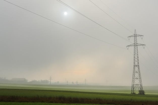 Enkele hoogspanningsmast met dichte mist en zon aan de hemel