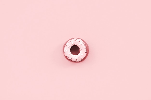 Enkele kleine plastic donut ligt op een pastel kleurrijke achtergrond.