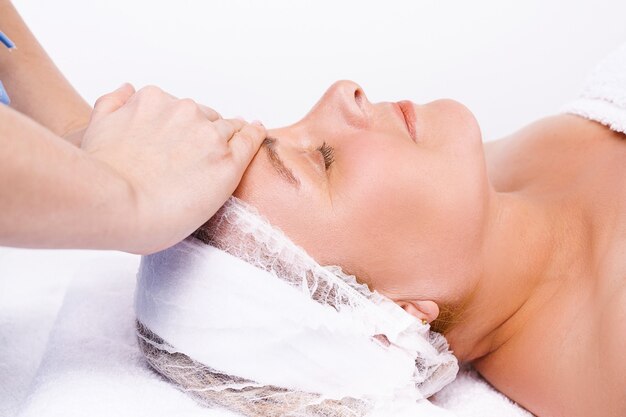 Enlarged photo. The hands of the master massage the face of an older woman. White background.