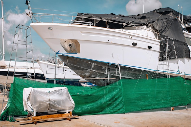 An enormous sailing yacht, covered with a black and green blanket, is under repair