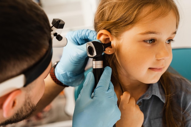 ENT doctor otolaryngologist looks through otoscope the ears of a little girl Otoscopy Treatment child ear pain