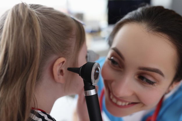 Ent woman examining ear of little girl with otoscope in clinic