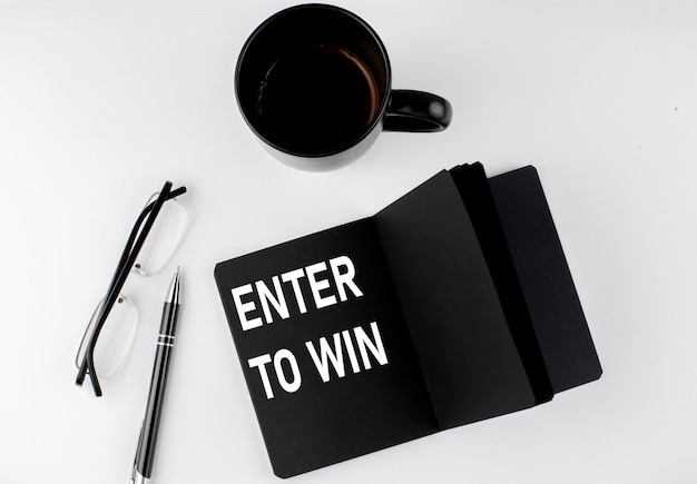 Enter to win written text in small black notebook with coffee\
pen and glasess on white background blackwhite style
