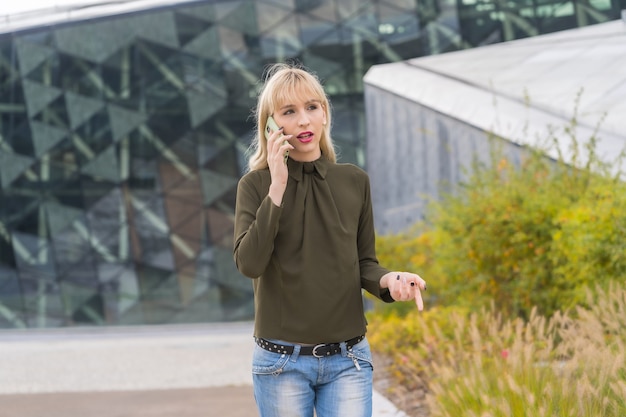 Enterprising Caucasian blonde girl in business park making work call, modern workplace among nature