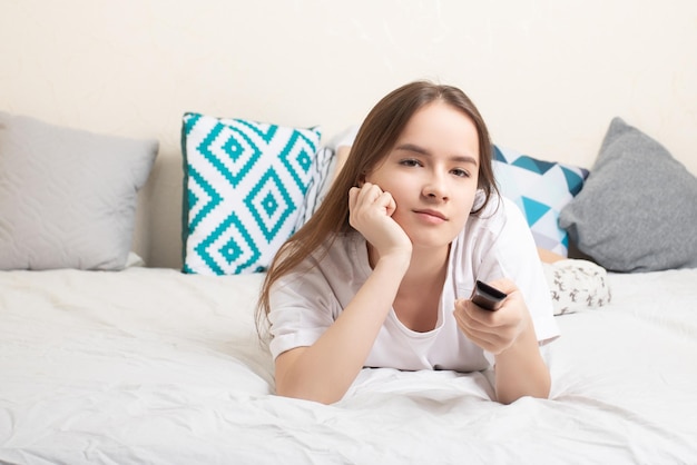 Entertaining television The girl lies at home on the bed with a remote control in her hands