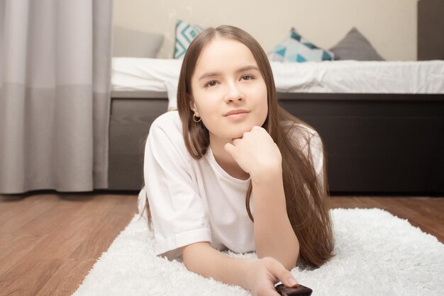 Entertaining television The girl lies at home on the carpet with a remote control in her hands