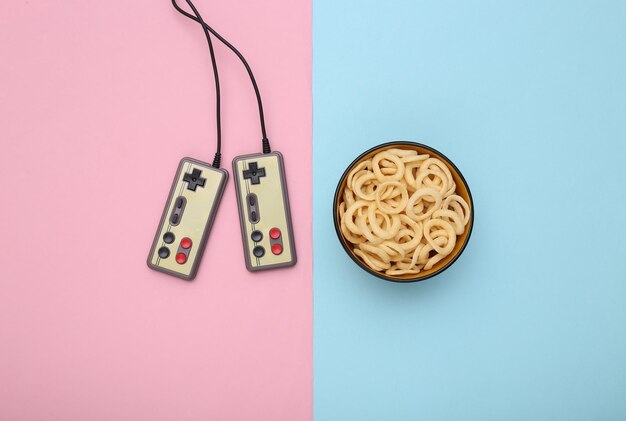 Entertainment time. gamepads and snack bowl on pink blue pastel background. top view