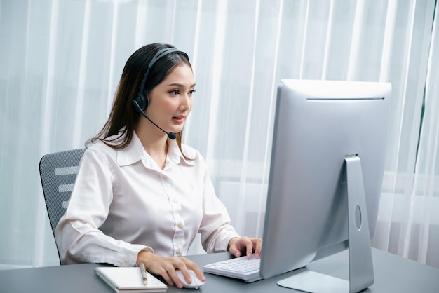 Enthousiaste Aziatische callcenter met headset en microfoon op haar laptop.