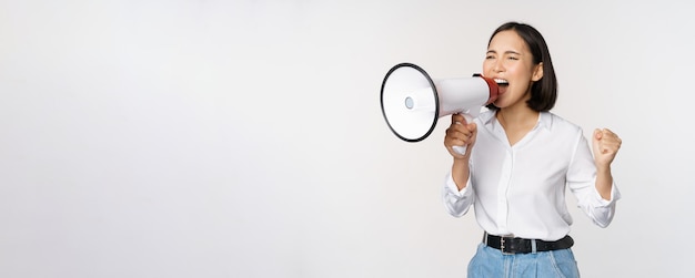 Enthousiaste Aziatische vrouw meisje activist schreeuwen tegen protest met behulp van megafoon op zoek zelfverzekerd praten in luidspreker protesteren staande op witte achtergrond