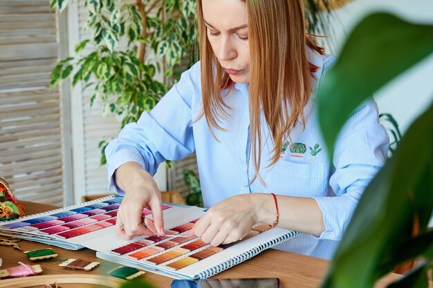 Enthousiaste blondine kiest de kleur van de draden om te borduren gebruikt het palet