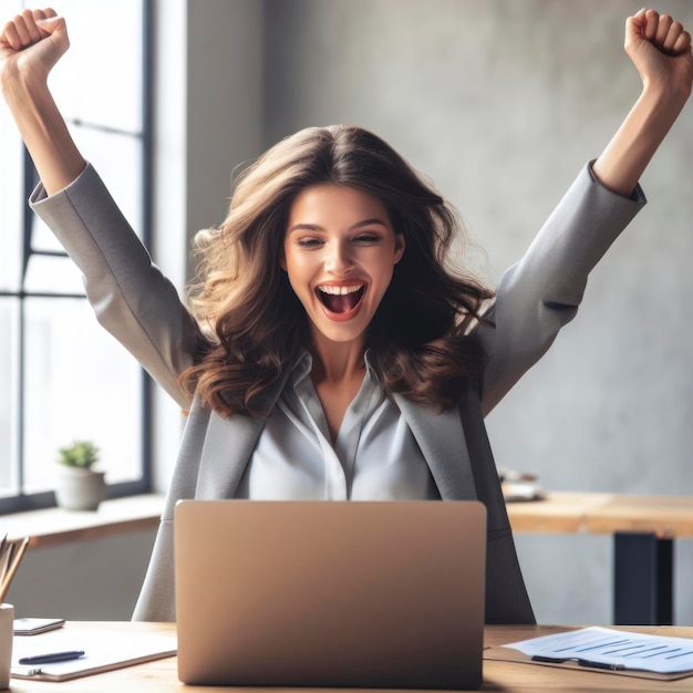 Enthousiaste jonge zakenvrouw houdt de armen omhoog en drukt positiviteit uit terwijl ze met een laptop werkt