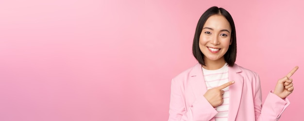 Enthousiaste professionele zakenvrouw verkoopster wijzende vingers naar rechts met advertentie of bedrijfslogo opzij poseren over roze achtergrond