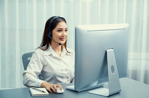 Enthusiastic asian call center with headset and microphone working on her laptop