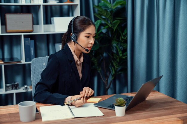 Enthusiastic asian call center with headset and microphone working on her laptop